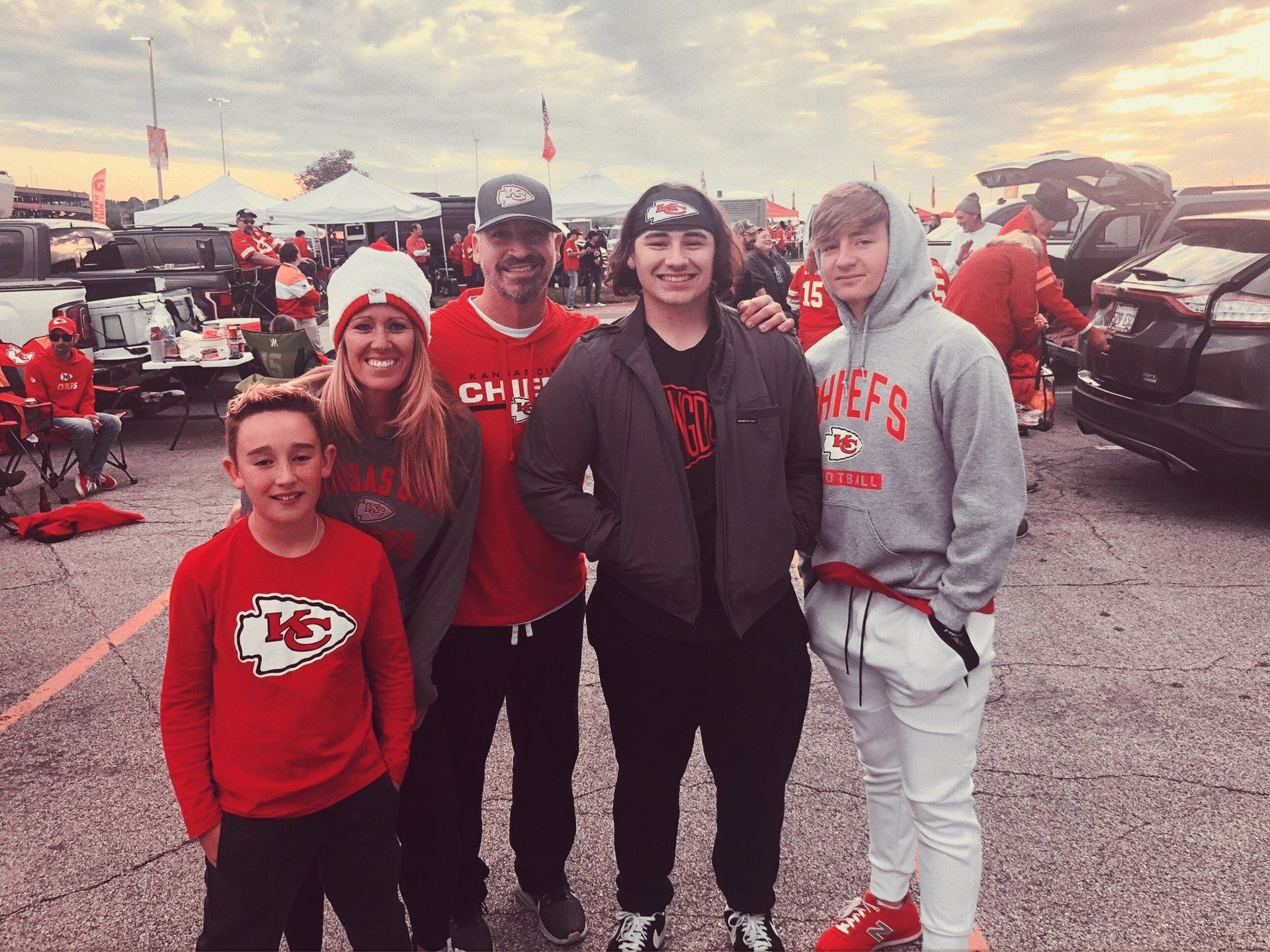 A group of five people wearing Kansas City Chiefs red apparel standing together in a stadium parking lot during a tailgate event.