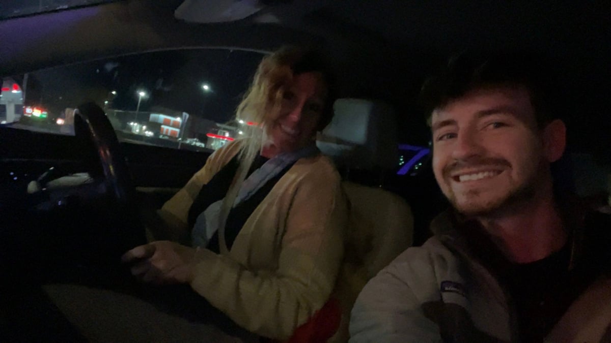 Two people smiling inside a car at night with city lights visible through the windows