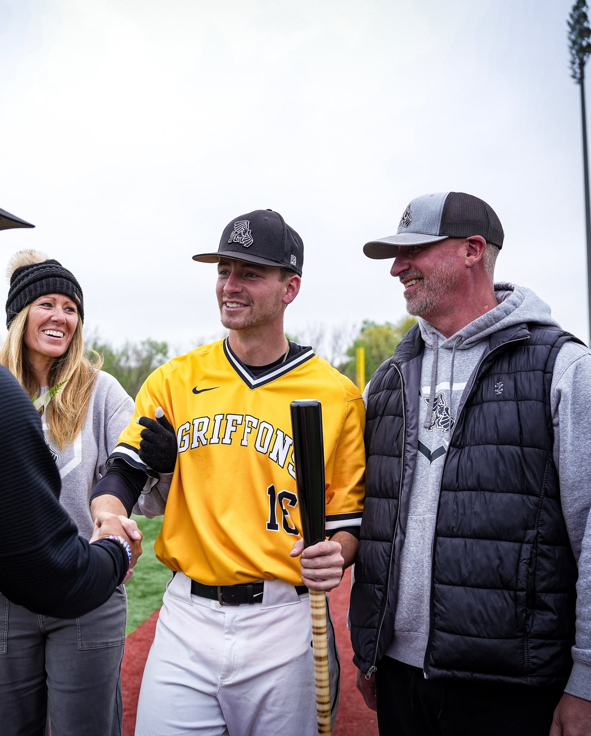 Baseball player in yellow Griffon uniform shaking hands with two people on a field