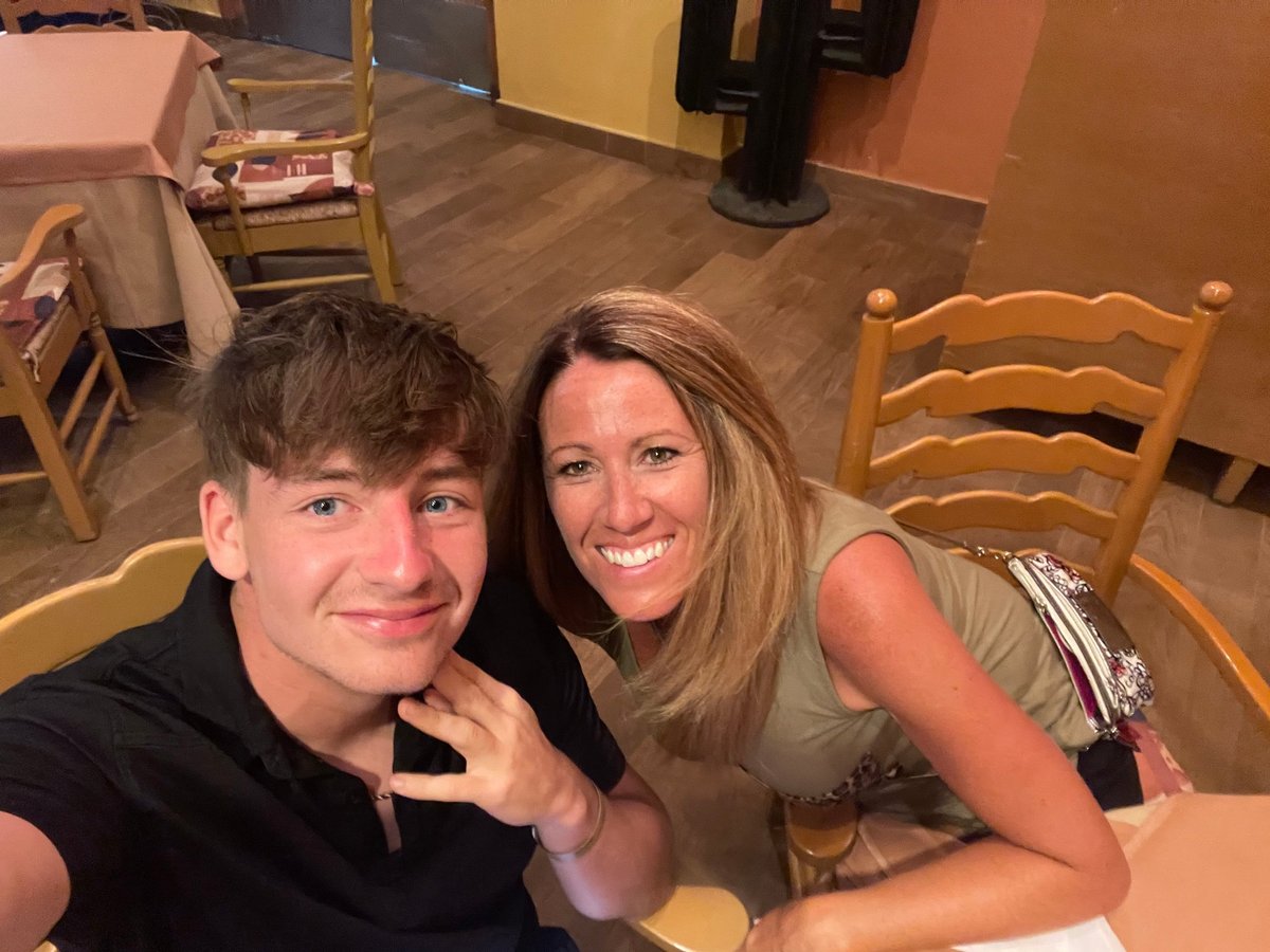 Young man and woman smiling at camera in casual indoor setting with wooden furniture
