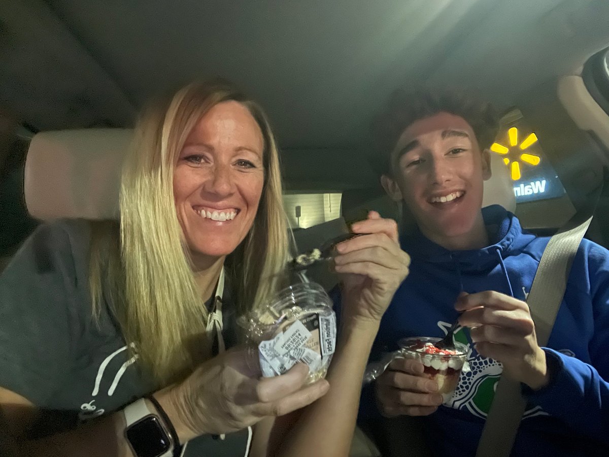 Two people smiling inside a car at night with a Walmart logo visible in the background