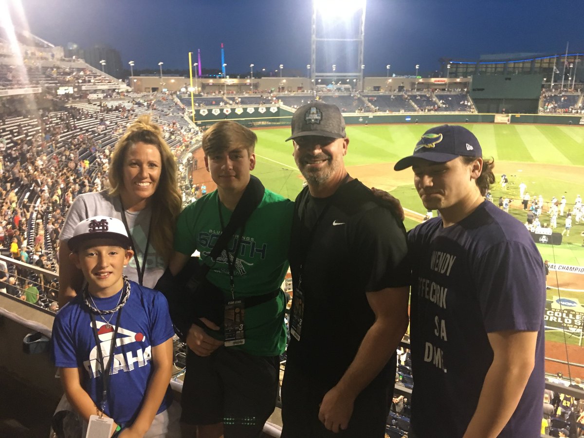 Group of five people posing together at a baseball stadium during a night game with crowded stands in the background