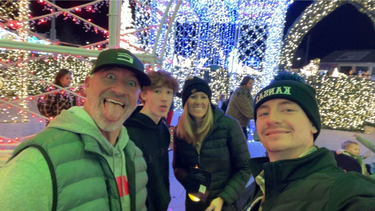 Group of four people smiling at a festive outdoor holiday light display at night