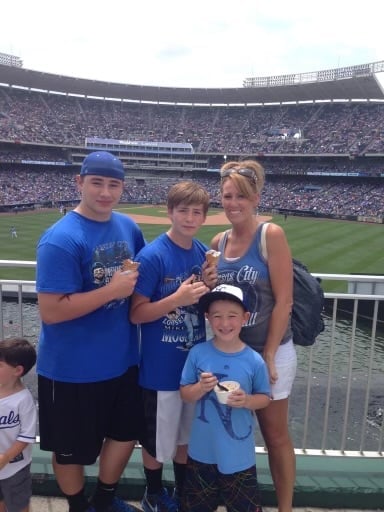 Family of four wearing blue sporting attire at a crowded baseball stadium during a game