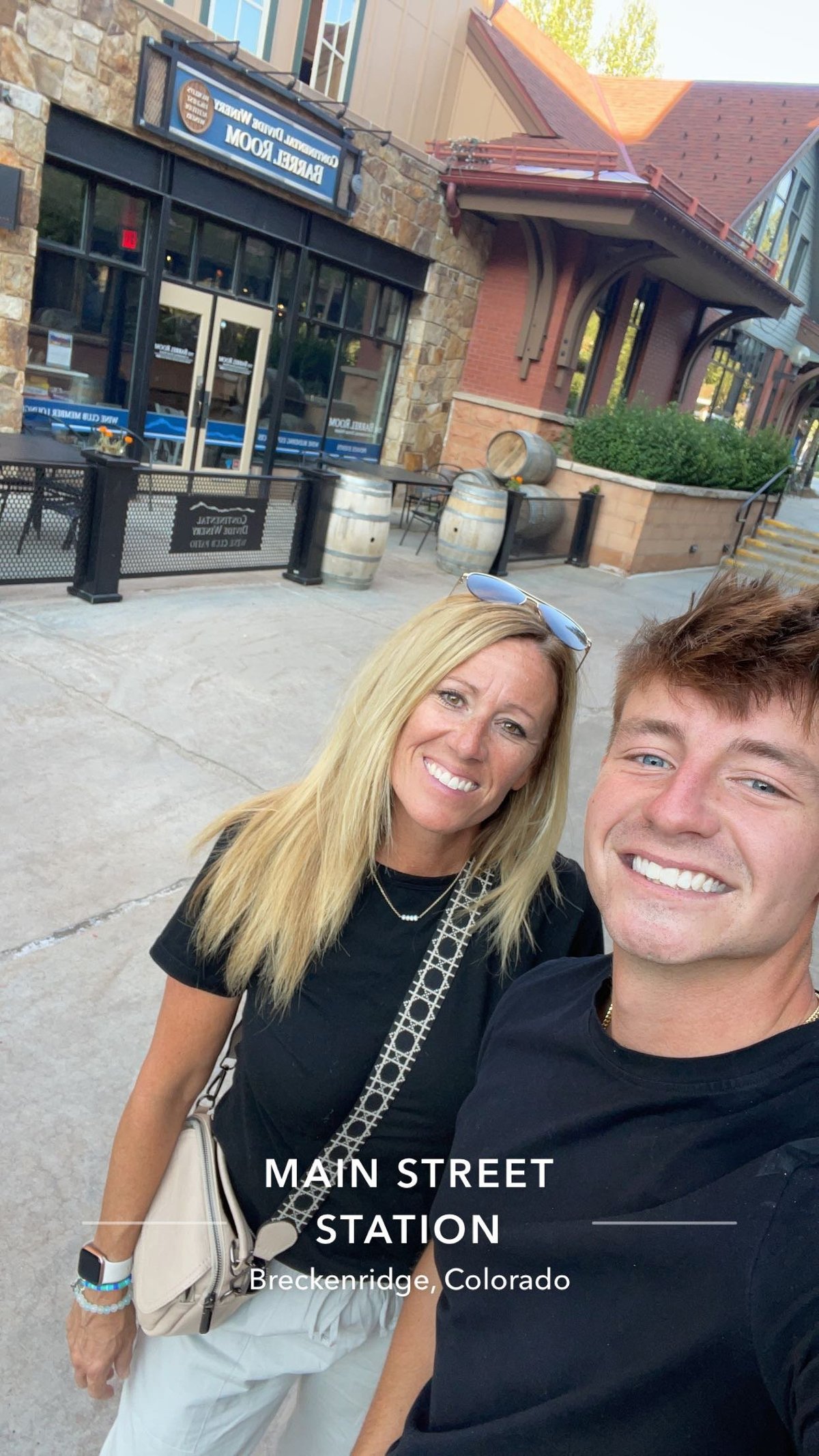 Two smiling people posing together on Main Street in Breckenridge, Colorado with historic storefronts and brick buildings in the background