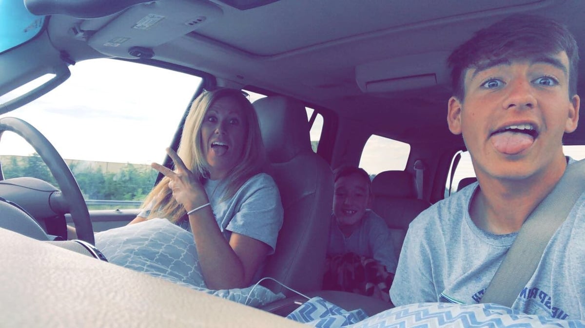 Two young people sitting in a car, smiling and making silly faces at the camera while driving on a sunny day