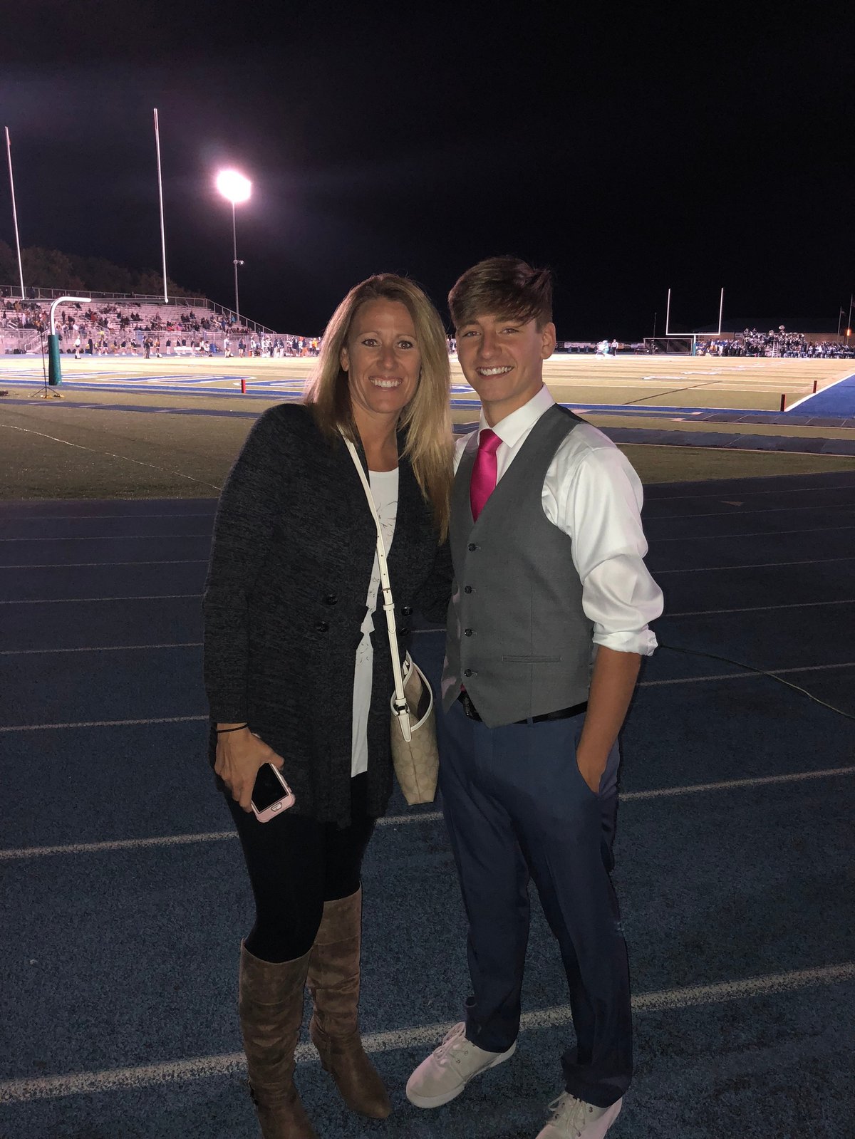 Two people posing together on an athletic field at night with stadium seating and lights visible in the background