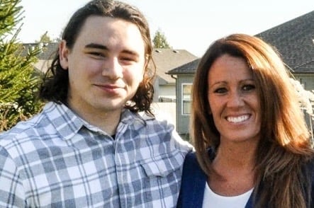 Two people smiling at camera outdoors with house and trees in background