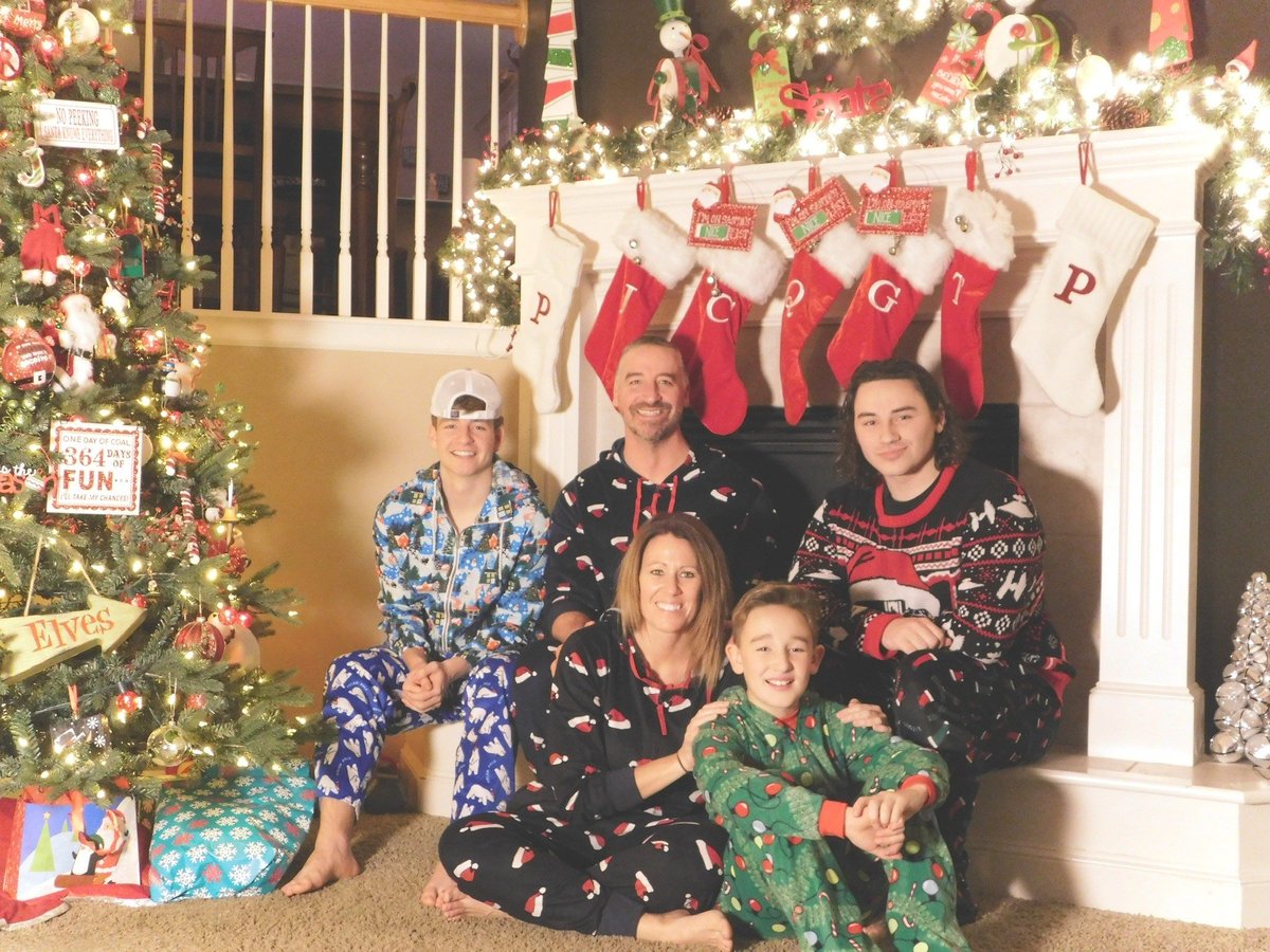 Family of five in pajamas posing in front of decorated Christmas fireplace with stockings and garland