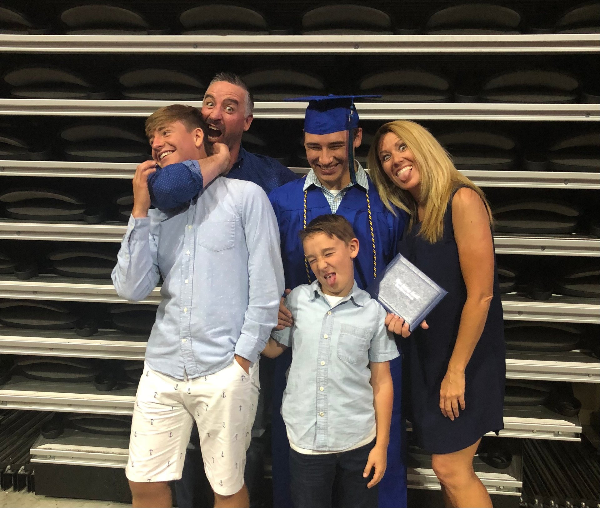 Family of five posing on bleachers, with a graduate in cap and gown holding a diploma
