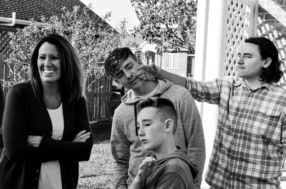 Black and white photo of a smiling woman with four people in a backyard setting with trees and houses in the background