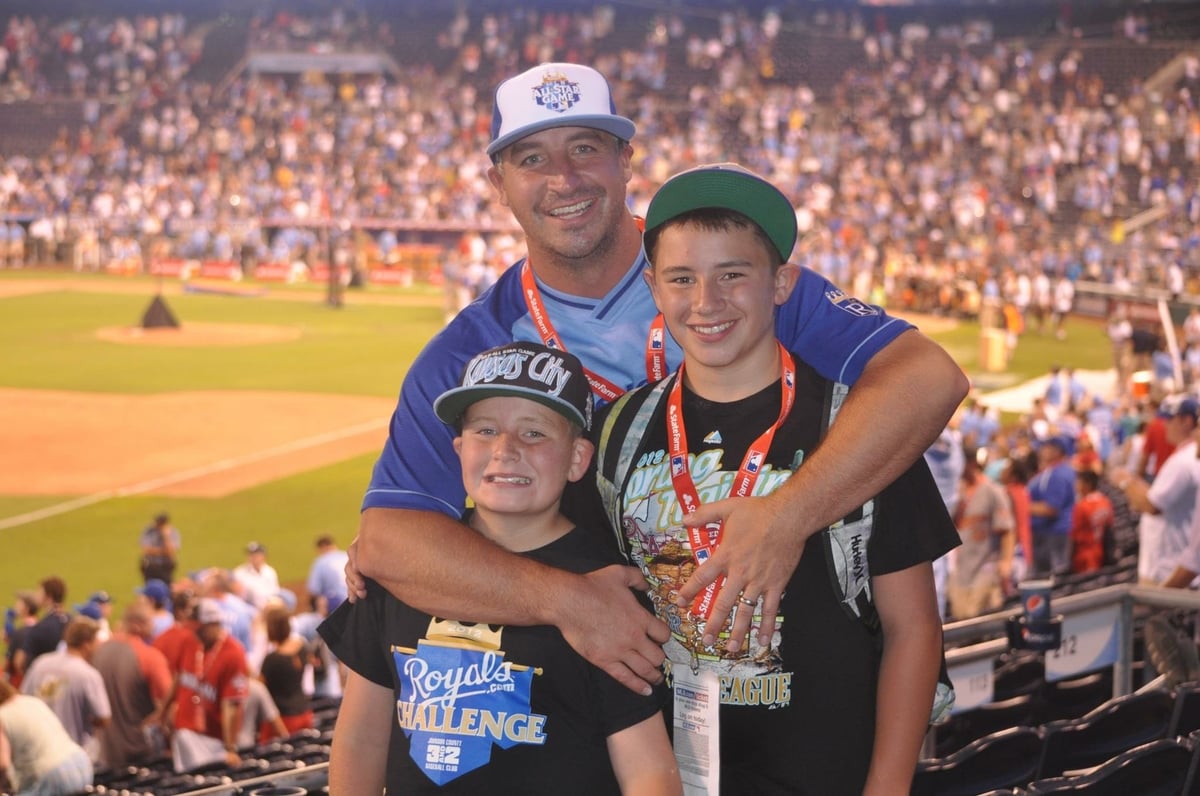 Three people posing together at a baseball stadium with crowded stands in the background